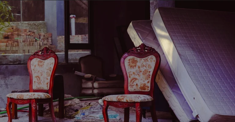 Mattress lean against a wall in a garage filled with other furniture that sits unused.